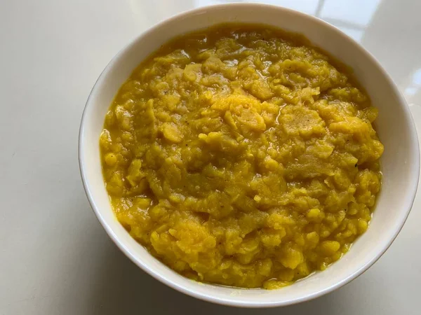 Yellow lentil dal gravy made with split pigeon peas in a white bowl on a white background