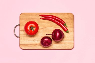 Sağlıklı beslenme. Kırmızı biberin yanında iki taze mor fiyonk ve tahta kesim tahtasında bir domates.