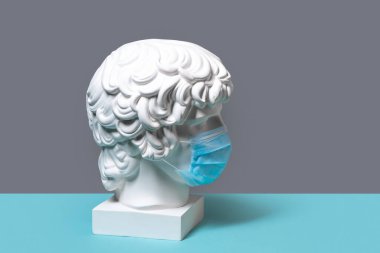 Antinous 'un başının gri arka planda tıbbi koruyucu maskeli beyaz alçıtaşı heykeli.