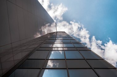Ofis binası gökyüzüne doğru uzanıyor. Bulutların ve mavi gökyüzünün yansımasında. Başarı, gelişme, motivasyon kavramı.