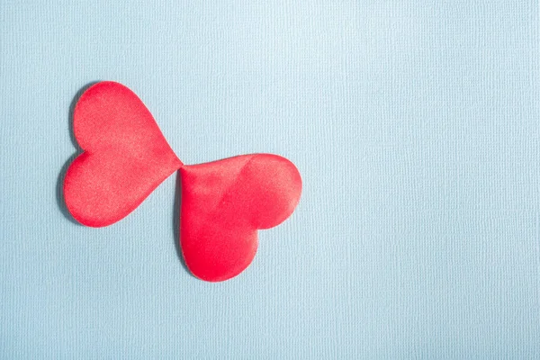 Two hearts on a blue texture background. The hearts touch each other and form a kind of butterfly.