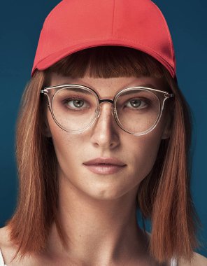Moda gözlük ve şapka ile çekici genç Kızıl saçlı kadın portresi. Kız kameraya bakıyor. Mavi arka plan.