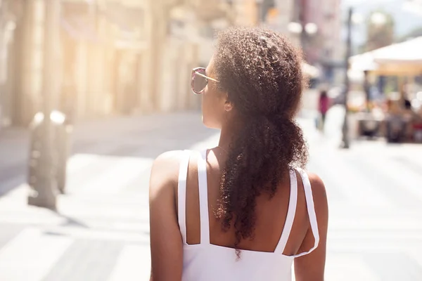Back view on beautiful african american girl with long curly hair walking on the italian street at sunny summer day. Leisure holiday time.