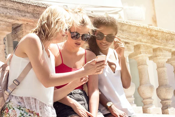 Güzel genç mutlu sarışın kız ve eğleniyor, gülümseyen çok ırklı Afrikalı-Amerikalı kadın. İtalya Yaz tatili. Güneşli bir gün birlikte vakit, cep telefonu arayan genç kız.
