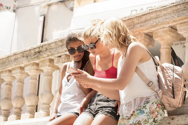 Güzel genç mutlu sarışın kız ve eğleniyor, gülümseyen çok ırklı Afrikalı-Amerikalı kadın. İtalya Yaz tatili. Güneşli bir gün birlikte vakit, cep telefonu arayan genç kız.
