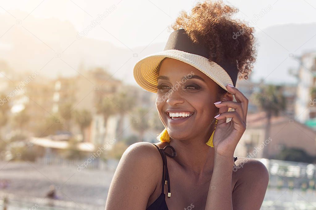 Beauty portrait of attractive young african american woman wearing yellow earrings and fashionable summer hat. Girl relaxing at italian coast.