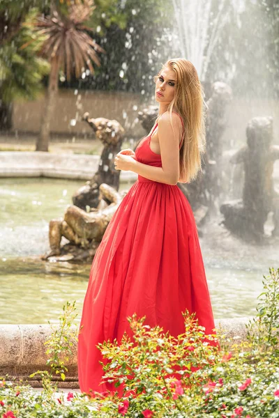 빨간색 맥시에 머리를 화려한 여자의 분수와 정원에서 드레스 — 스톡 사진