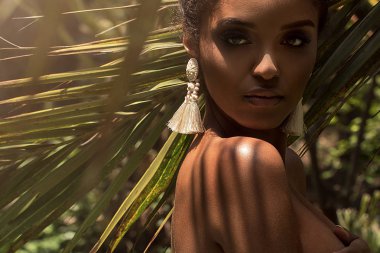 Palm üzerinde poz tek küpe, giyen güzel Afrikalı-Amerikalı kadın tropikal sürgün bırakır.