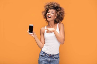 Hareket eden telefon tutarak ve sarı arka plan üzerinde duran boş ekranda gösterilen gülümseyen güzel bir Afrikalı kadınla afro saç modeli, fotoğrafı.