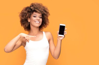 Hareket eden telefon tutarak ve sarı arka plan üzerinde duran boş ekranda gösterilen gülümseyen güzel bir Afrikalı kadınla afro saç modeli, fotoğrafı.