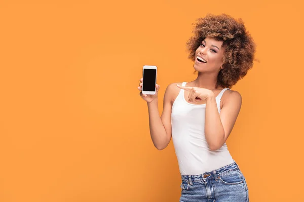 女性の写真笑顔美しいアフリカ アフロの髪型で携帯電話を保持していると 黄色の背景の上に立って 空白の画面上に表示 — ストック写真