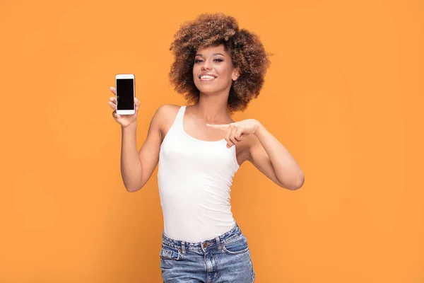 女性の写真笑顔美しいアフリカ アフロの髪型で携帯電話を保持していると 黄色の背景の上に立って 空白の画面上に表示 — ストック写真