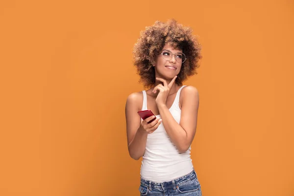 アフロの髪型と黄色の背景の上に立って 携帯電話を保持しているに対応する笑みを浮かべて美しいアフリカ女性の写真 — ストック写真
