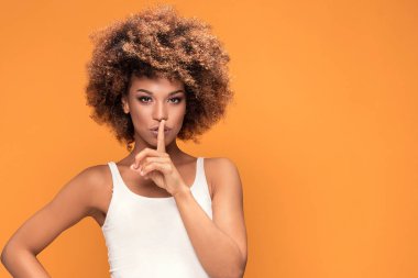 Genç afro kadın parmağı ağız, sarı arka plan üzerinde tutulması.