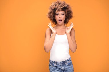 Kameraya bakarak hayran güzel afro kadın şaşırttı. Sarı arka plan üzerinde poz kız.