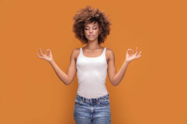 Sakin güzel afro kadın sarı arka planda, meditasyon poz poz.