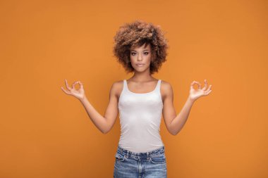 Sakin güzel afro kadın sarı arka planda, meditasyon poz poz.