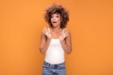 Sürpriz hayran güzel afro kadın kameraya, seyir gülümseyerek. Sarı arka plan üzerinde poz kız.