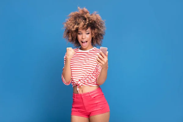 アフロの髪型と携帯電話と青い背景の上に立って撮影 Selfie を保持に対応する笑みを浮かべて美しいアフリカ女性の写真 — ストック写真
