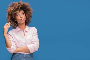 Gür saçlı tutan moda gözlük ve düşünme, mavi renkli Afro Amerikan kadın portresi.