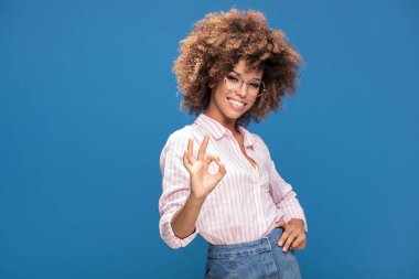 Gür saç moda gözlük, mavi arka plan üzerinde gülümseyen Afro Amerikan kadın portresi.