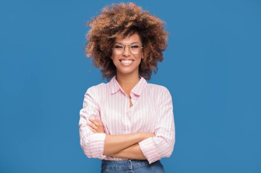 Afro Amerikalı kadın moda gözlük takıyor, kameraya bakıyor ve gülümsüyor, mavi arka plan gür saçlı closeup portresi.