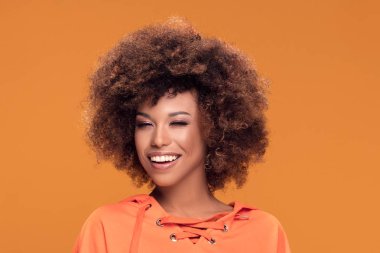 Kamera, sarı arka plan göz kırpıyor mutlu gülümseyen afro kadın portresi.