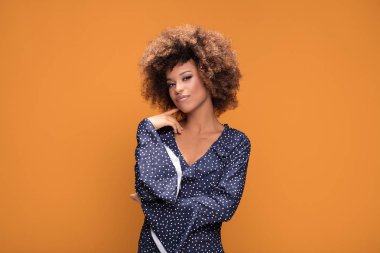 Gülümseyerek, sarı arka plan üzerinde duran moda noktalı elbiseyle poz mutlu güzel Afrikalı-Amerikalı kadın.