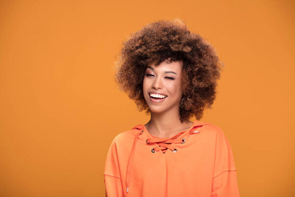 Portrait of happy smiling afro woman winking to the camera, yellow background.