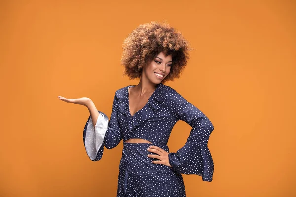 Gülümseyerek, sarı arka plan üzerinde duran moda noktalı elbiseyle poz mutlu güzel Afrikalı-Amerikalı kadın.