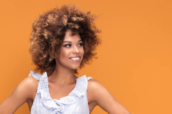 Beauty portrait of smiling african american young woman with afro hairstyle posing on yellow background.