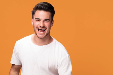 Kameraya, sarı stüdyo arka plan üzerinde poz arayan genç yakışıklı adam onun başarı zevk gülümseyen.