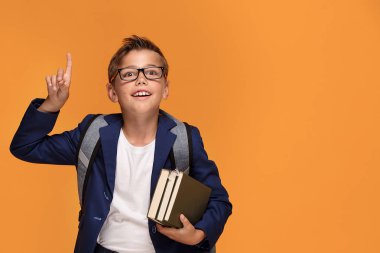 Kitap, okul çocuğu ile sırt çantası ayakta turuncu arka plan üzerinde gözlük gülümseyen.