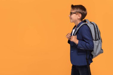 Okul çocuğu ile sırt çantası ayakta turuncu arka plan üzerinde gözlük gülümseyen.