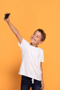 Stüdyo çekim Genç beyaz küçük çocuğun tarafından cep telefonu sarı stüdyo arka plan karşı selfie portre çekici.