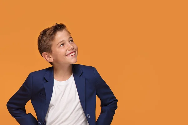 Little elegant boy smiling on orange studio background, a lot of copy space.