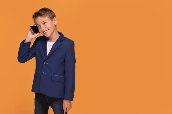 オレンジ スタジオの背景 コピー スペースでスマート フォンを持った少年 大人のビジネスマンの再生フォーマルなスーツで幸せな子 — ストック写真