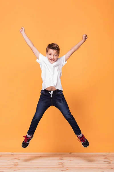 小さな学校の男の子黄色の背景でスタジオでジャンプします 幸せな子供時代の概念 — ストック写真