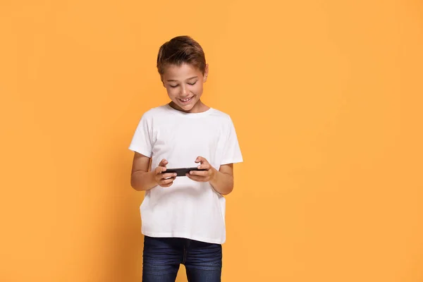工作室拍摄年轻的白种小男孩使用手机对黄色演播室背景 — 图库照片
