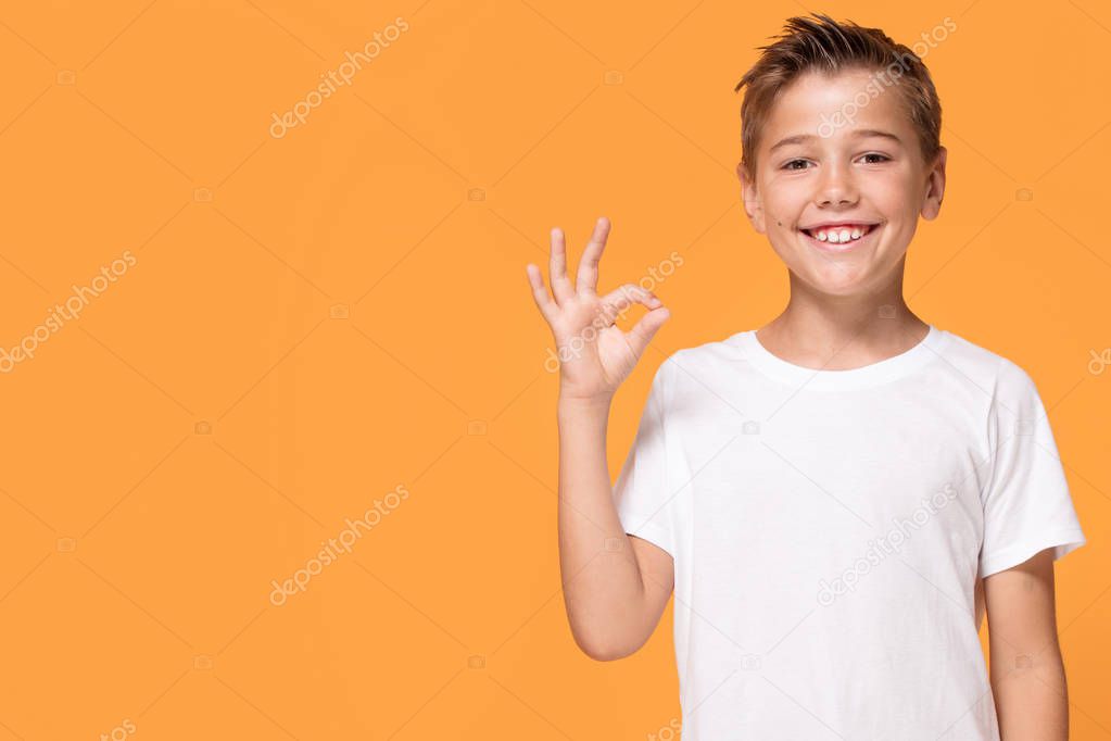 Young emotional handsome boy standing on orange studio background. Human emotions, facial expression concept.