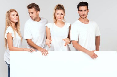 Bir grup insan ile birlikte boş beyaz tahta poz beyaz gömlek giymiş genç çok etnik gruptan oluşan güzel. Çarklı gülümseyen arkadaşlar.