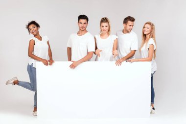 Bir grup insan ile birlikte boş beyaz tahta poz beyaz gömlek giymiş genç çok etnik gruptan oluşan güzel. Çarklı gülümseyen arkadaşlar.
