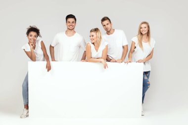 Bir grup insan ile birlikte boş beyaz tahta poz beyaz gömlek giymiş genç çok etnik gruptan oluşan güzel. Çarklı gülümseyen arkadaşlar.