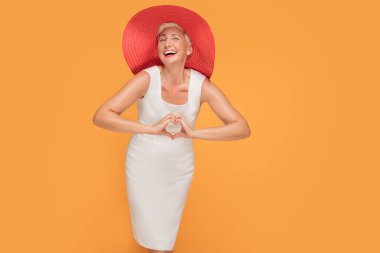 Kameraya bakarak ve gülümseyerek poz sarı stüdyo arka plan üzerinde kırmızı yaz şapka giyen orta yaş güzel kadın.