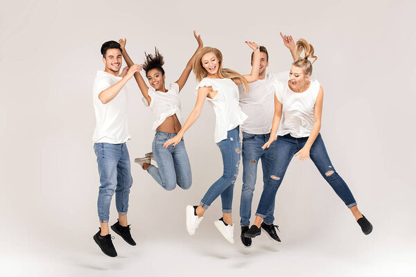 Group of young multi-ethnic attractive people wearing white shirts, smiling and having fun together, jumping in studio.