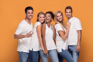 Turuncu studio arka planda beyaz casual gömlek poz kameraya gülümseyen beş genç etnik insanlar.