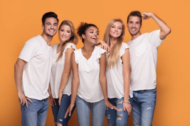 Turuncu studio arka planda beyaz casual gömlek poz kameraya gülümseyen beş genç etnik insanlar.