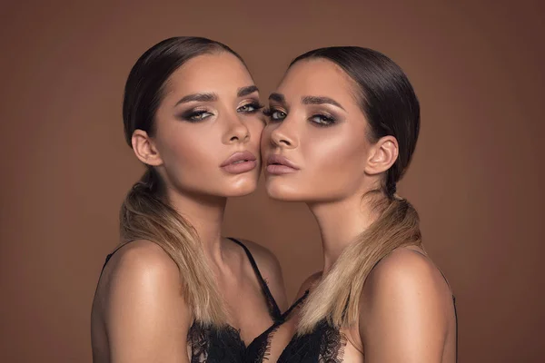 Beauty and femininity concept. Two attractive twins women in glamour makeup. Portrait photo.