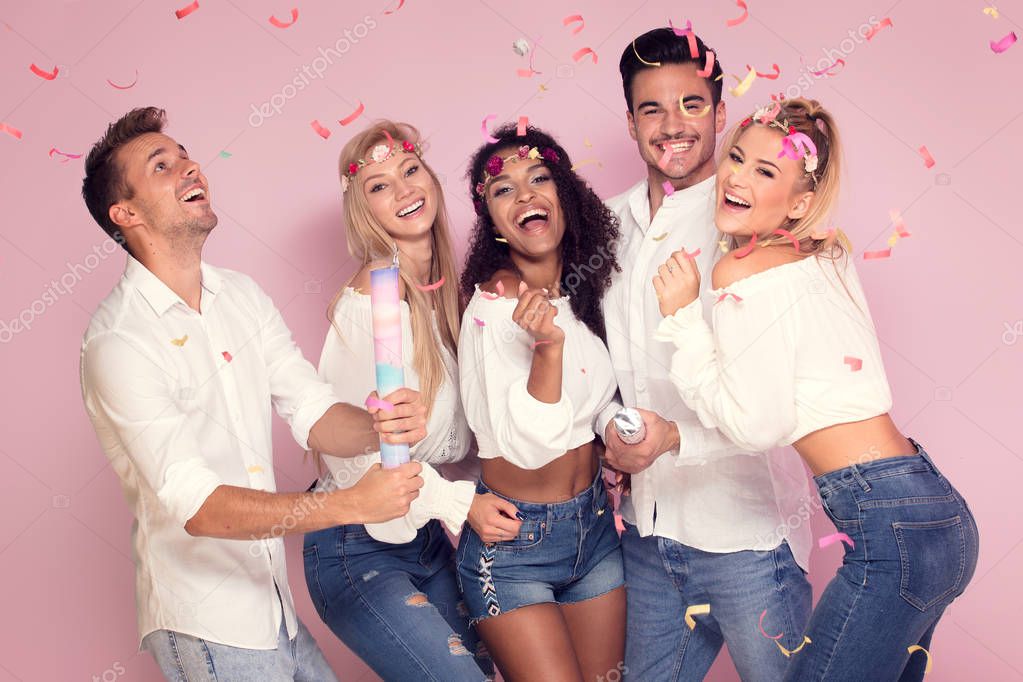 Group of beautiful young people partying together, posing on pink studio background.