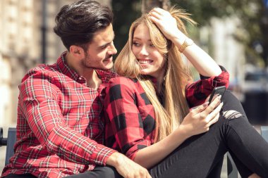 Aşk açık havada kalma çift gülümsüyor. Oturmuş, cep telefonu arayan genç mutlu çift.